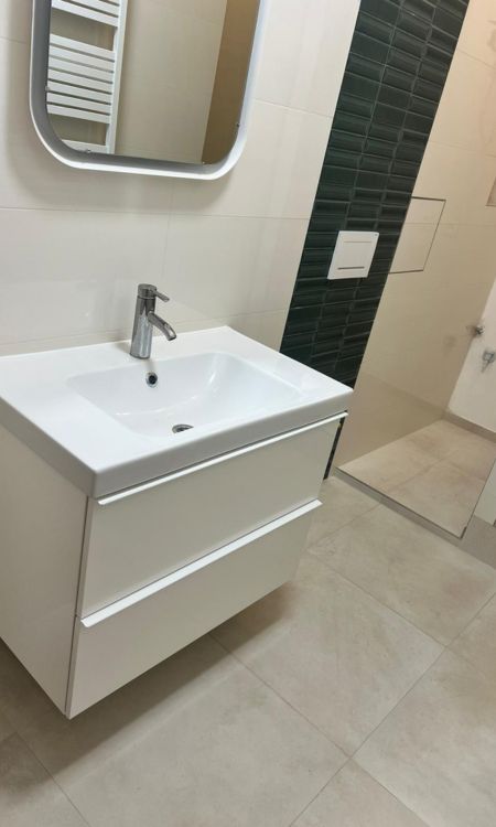 Nové umyvadlo s podsvíceným zrcadlemv nové koupelně se zelenými kachličkami